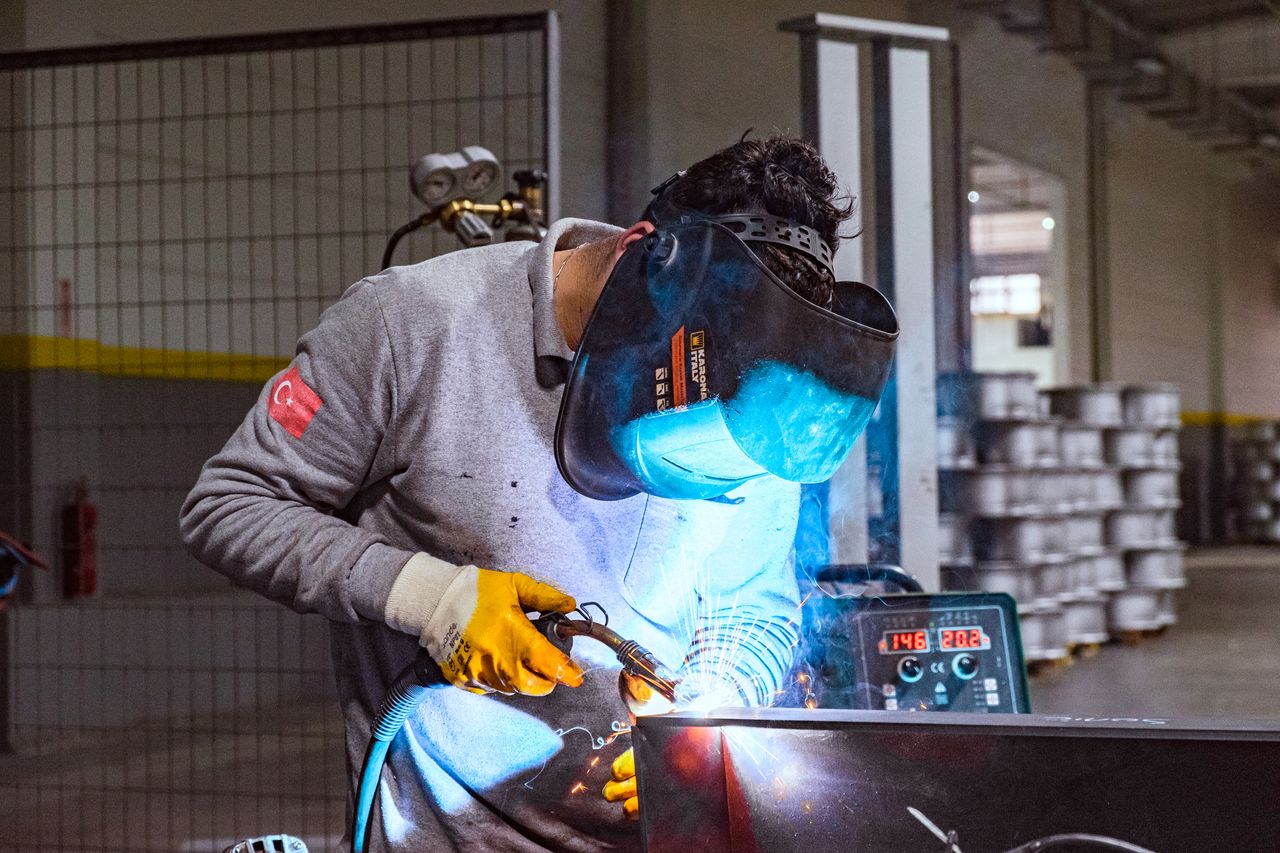 A welder wearing protective gear works in an industrial workshop, showcasing skill and focus.