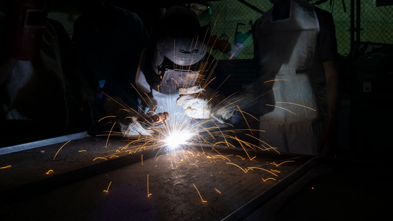 Skilled welder in protective gear creating sparks in a dark workshop environment.